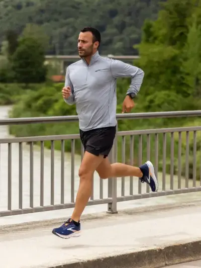 Man running along a sidewalk while wearing a pair of Brooks running shoes