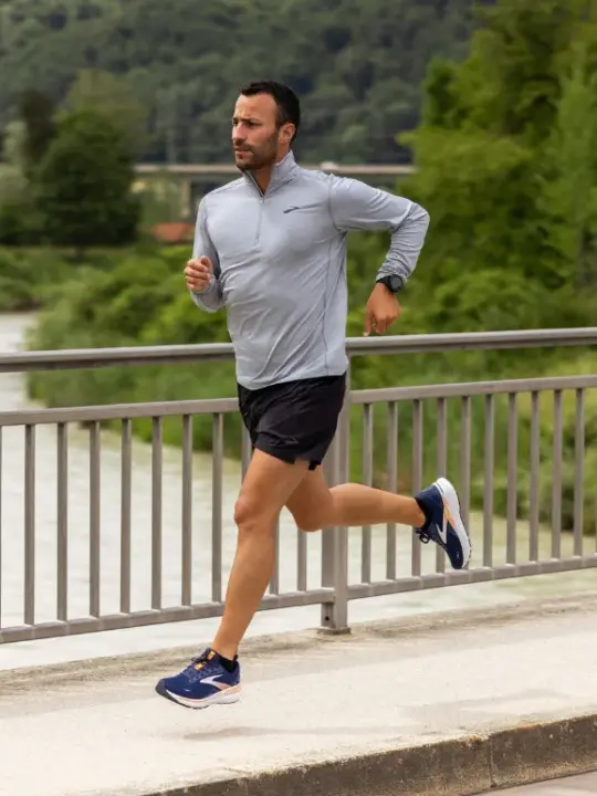 Man running along a sidewalk while wearing a pair of Brooks running shoes