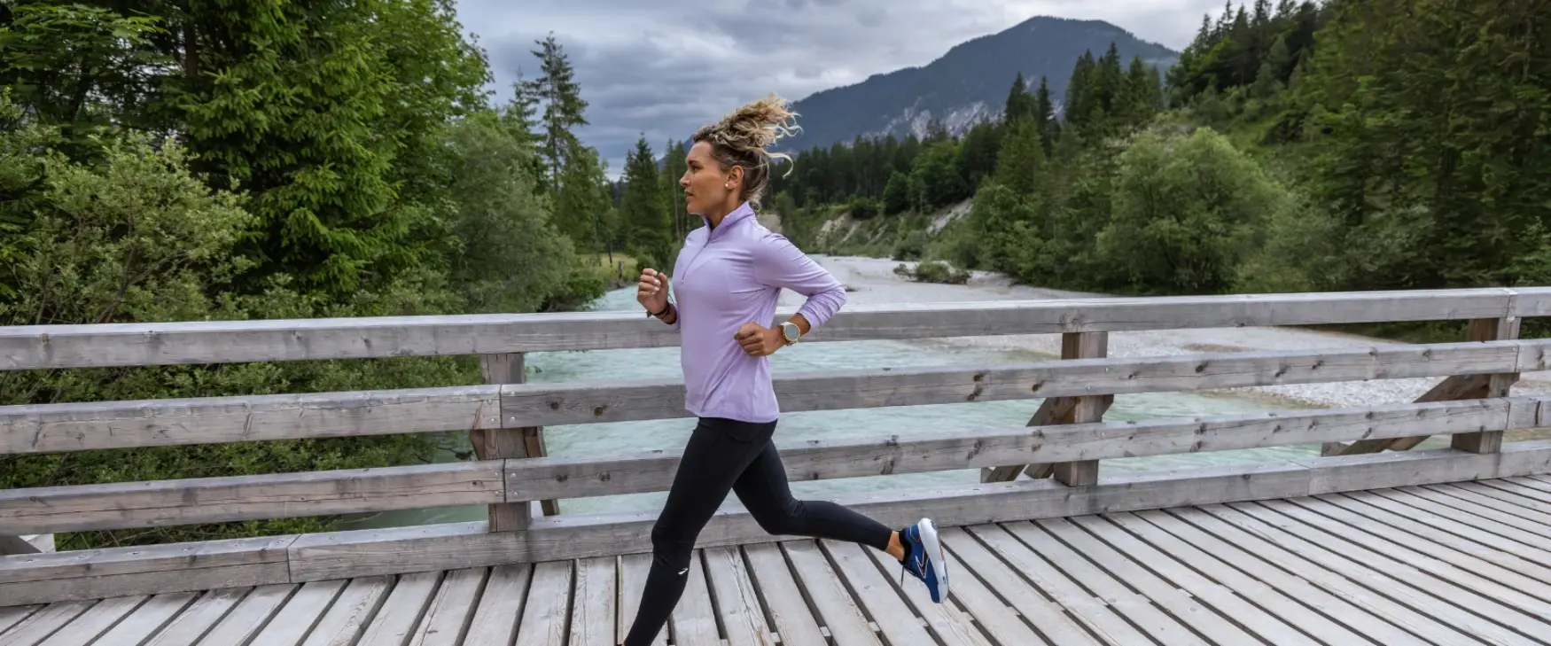 Woman running along a bridge in with mountains and greenery surrounding her
