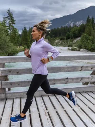 Woman running along a bridge in with mountains and greenery surrounding her